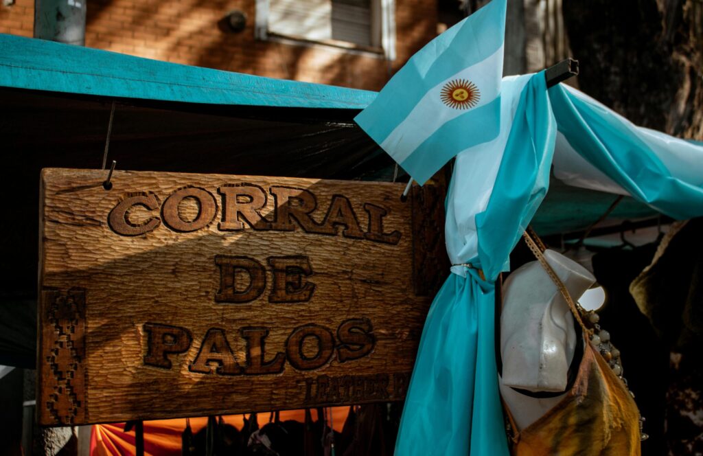 Wooden 'Corral de Palos' sign with Argentinian flag at a Buenos Aires market.